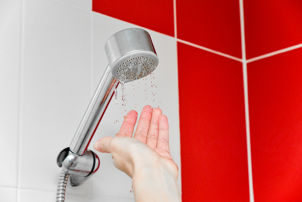 A person taking a shower with low water pressure, with only a few drops of water falling from the showerhead.